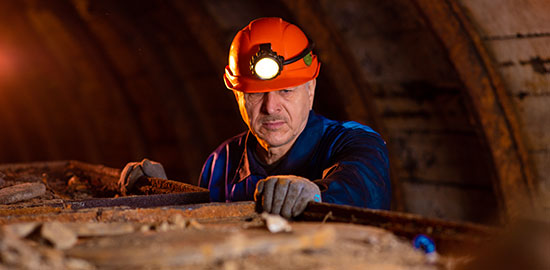Ein Arbeiter mit Stirnlampe &uuml;berpr&uuml;ft Material in einer unterirdischen Arbeitsumgebung.