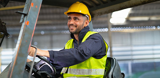 Ein Arbeiter mit Helm und Warnweste bedient einen Radlader in einer Industriehalle.