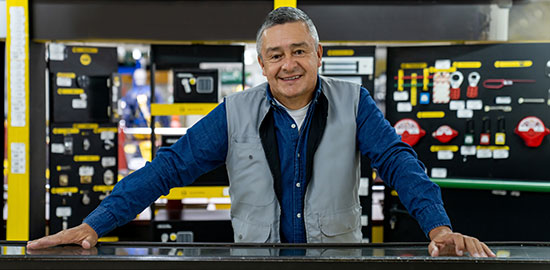 Ein Mitarbeiter steht hinter einem Verkaufstresen und l&auml;chelt, im Hintergrund sind technische Produkte ausgestellt.