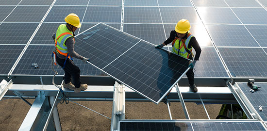 Zwei Arbeiter installieren ein Solarpanel auf einem Dach einer gro&szlig;en Photovoltaikanlage.