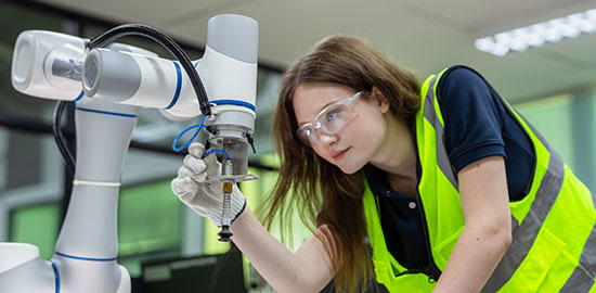 Eine Fachkraft mit Schutzbrille arbeitet an einem industriellen Roboterarm in einer Werkstatt.