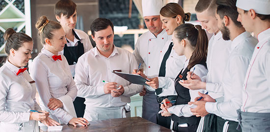 Mehrere Mitarbeitende aus K&uuml;che und Service besprechen gemeinsam Abl&auml;ufe in einem Restaurant.