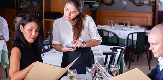 Eine Servicekraft ber&auml;t G&auml;ste am Tisch und nimmt eine Bestellung in einem Restaurant auf.