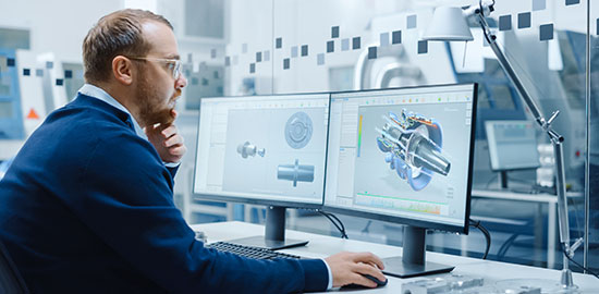 Ein Mitarbeiter erstellt am Computer technische Zeichnungen und 3D-Modelle von Maschinenbauteilen.