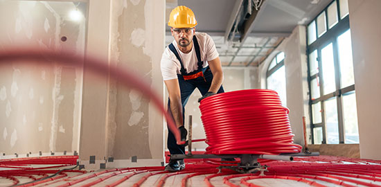 Ein Handwerker verlegt Rohre f&uuml;r eine Fu&szlig;bodenheizung in einem Geb&auml;ude.