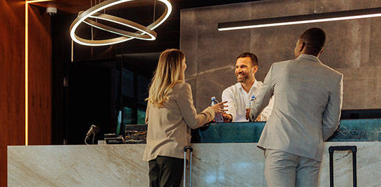 G&auml;ste sprechen mit einem Mitarbeiter am Empfang eines Hotels und checken ein.