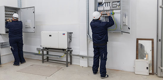 Zwei Elektriker arbeiten an ge&ouml;ffneten Schaltschr&auml;nken und installieren elektrische Komponenten.