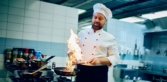Ein Koch bereitet ein Gericht in einer professionellen K&uuml;che zu und flambiert eine Pfanne.