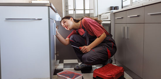 Eine Handwerkerin &uuml;berpr&uuml;ft ein Ger&auml;t in einer K&uuml;che und f&uuml;hrt eine Reparatur durch.