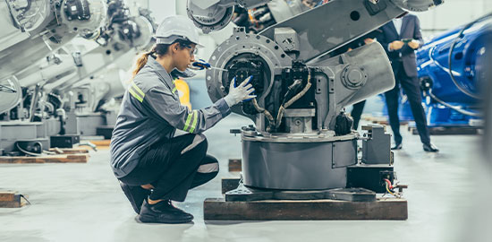 Eine Mitarbeiterin &uuml;berpr&uuml;ft eine industrielle Maschine in einer Produktionshalle.