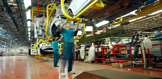 Arbeiter montieren Fahrzeuge an einer Produktionslinie in einer Industriehalle.