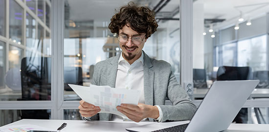 Ein Mitarbeiter sitzt am Schreibtisch und pr&uuml;ft Dokumente in einem B&uuml;ro.