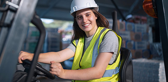 Eine Mitarbeiterin f&auml;hrt ein Transportfahrzeug im Lager und blickt zur Kamera.