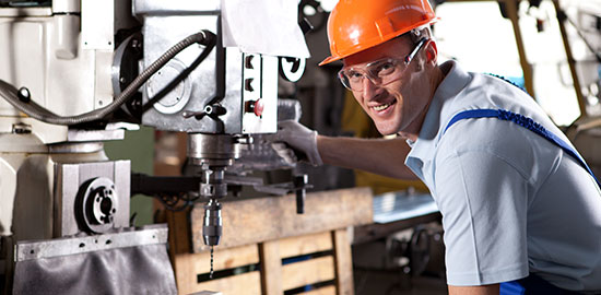 Ein Arbeiter bedient eine Metallmaschine und bearbeitet ein Werkst&uuml;ck in einer Werkstatt.