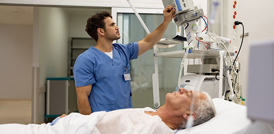 Ein Pfleger stellt medizinische Ger&auml;te ein, w&auml;hrend ein Patient im Krankenhausbett liegt.