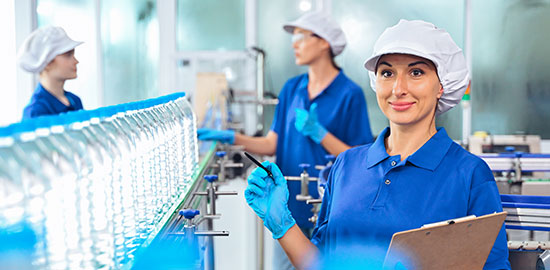 Eine Mitarbeiterin mit Schutzkleidung kontrolliert Flaschen an einer laufenden Produktionslinie.