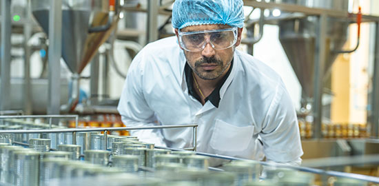 Ein Mitarbeiter in Schutzkleidung &uuml;berpr&uuml;ft Produkte an einer Produktionsanlage.