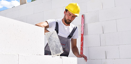 Ein Handwerker setzt Steine und tr&auml;gt M&ouml;rtel beim Bau einer Wand auf.