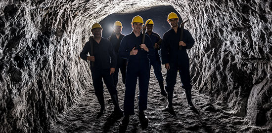 Eine Gruppe von Bergarbeitern steht mit Schutzhelmen in einem unterirdischen Tunnel.