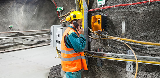 Ein Arbeiter &uuml;berpr&uuml;ft technische Anlagen und spricht dabei &uuml;ber Funk in einem Tunnel.