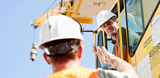 Zwei Bauarbeiter kommunizieren an einer gro&szlig;en Baumaschine auf einer Baustelle.