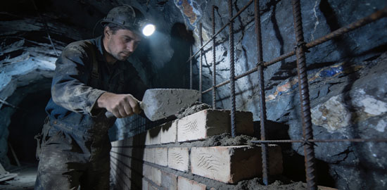 Ein Arbeiter mauert eine Wand in einem unterirdischen Stollen und tr&auml;gt M&ouml;rtel auf.