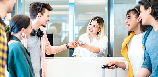 Eine Mitarbeiterin &uuml;bergibt einem Kunden eine Karte am Empfang, w&auml;hrend weitere Personen warten.
