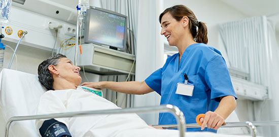 Eine Pflegekraft betreut eine Patientin im Krankenhausbett und spricht beruhigend mit ihr.