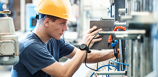 Ein Facharbeiter arbeitet an einer industriellen Maschine und bearbeitet Metallbauteile.