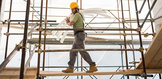 Ein Handwerker tr&auml;gt Baumaterial &uuml;ber ein Ger&uuml;st auf einer Baustelle.