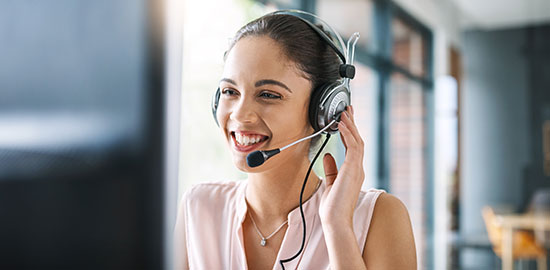 Eine Mitarbeiterin spricht mit einem Headset am Computer und betreut Kunden.